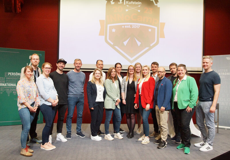 Zu sehen ist das Jurorenteam des INNoCamp. Sie stehen gemeinsam auf einer Bühne. Im Hintergrund befindet sich eine Leinwand mit dem INNoCamp-Logo. | © FH Kufstein Tirol