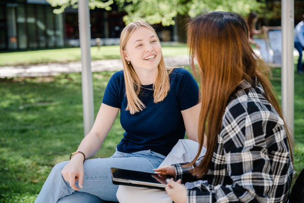 Zwei Frauen sitzen im Park und halten eine fröhliche Konversation miteinander. | © FH Kufstein Tirol