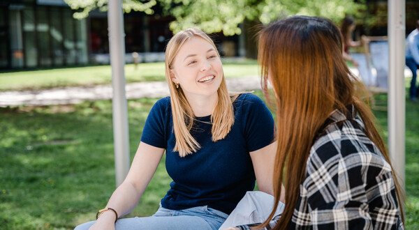 Zwei Frauen sitzen im Park und halten eine fröhliche Konversation miteinander. | © FH Kufstein Tirol