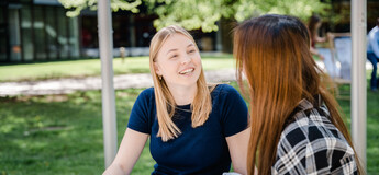 Zwei Frauen sitzen im Park und halten eine fröhliche Konversation miteinander. | © FH Kufstein Tirol