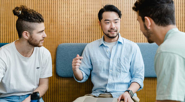 Drei Studierende im Gespräch bei Gruppenarbeit mit Laptop in moderner Sitzecke