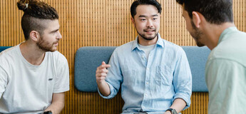 Drei Studierende im Gespräch bei Gruppenarbeit mit Laptop in moderner Sitzecke